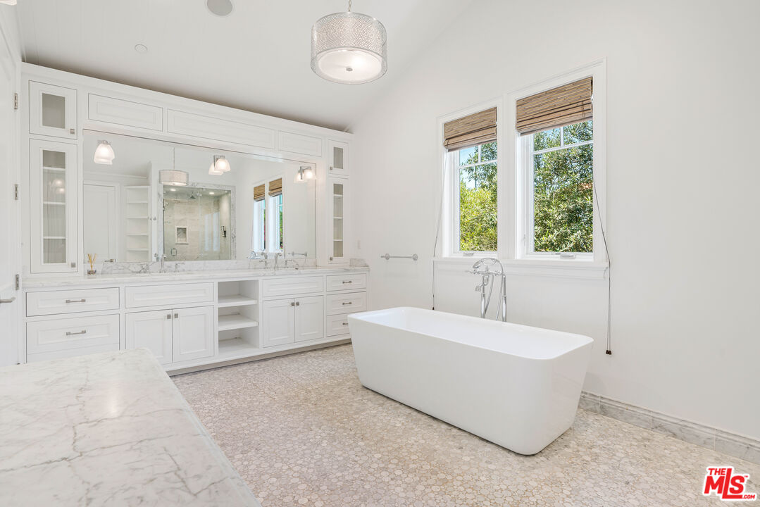 Bathroom with a freestanding soaking tub beneath two windows and a long marble vanity.