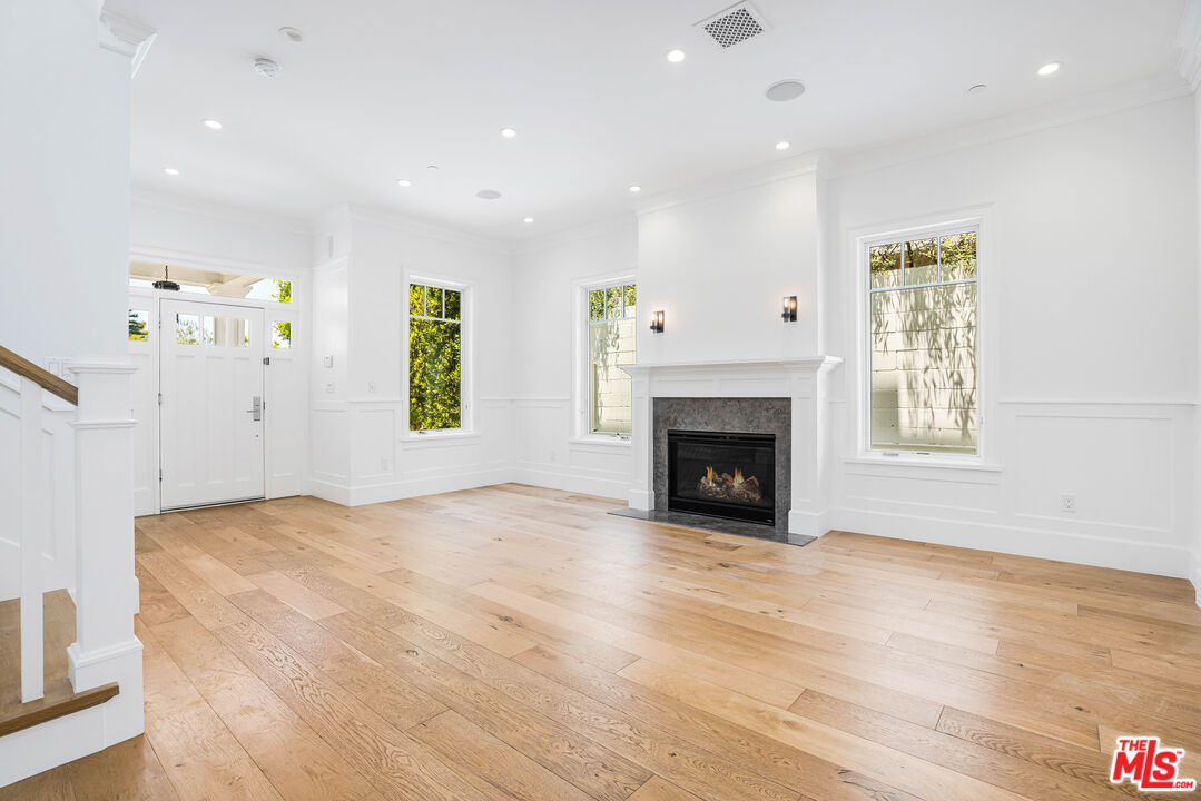 Vacant living room with pale wood floors, tall windows, and a fireplace with a gray stone surround.