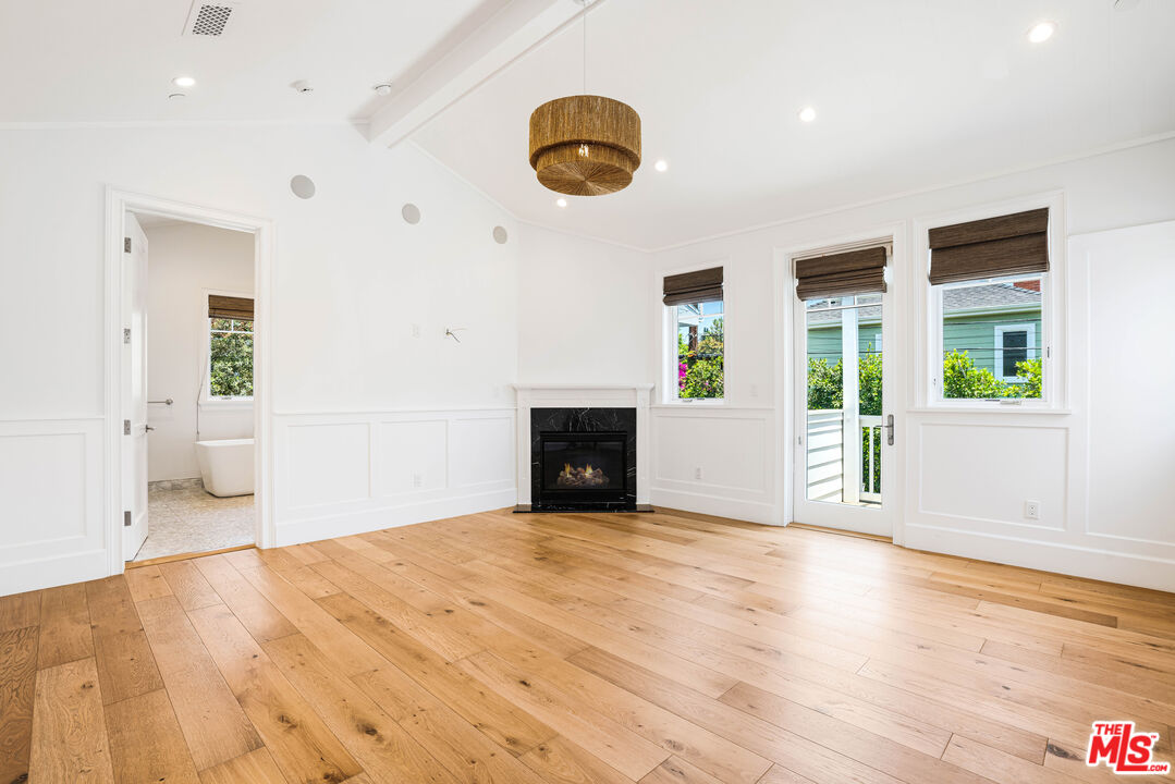 Vacant living room with a black fireplace, wide-plank wood floors, and windows overlooking greenery.