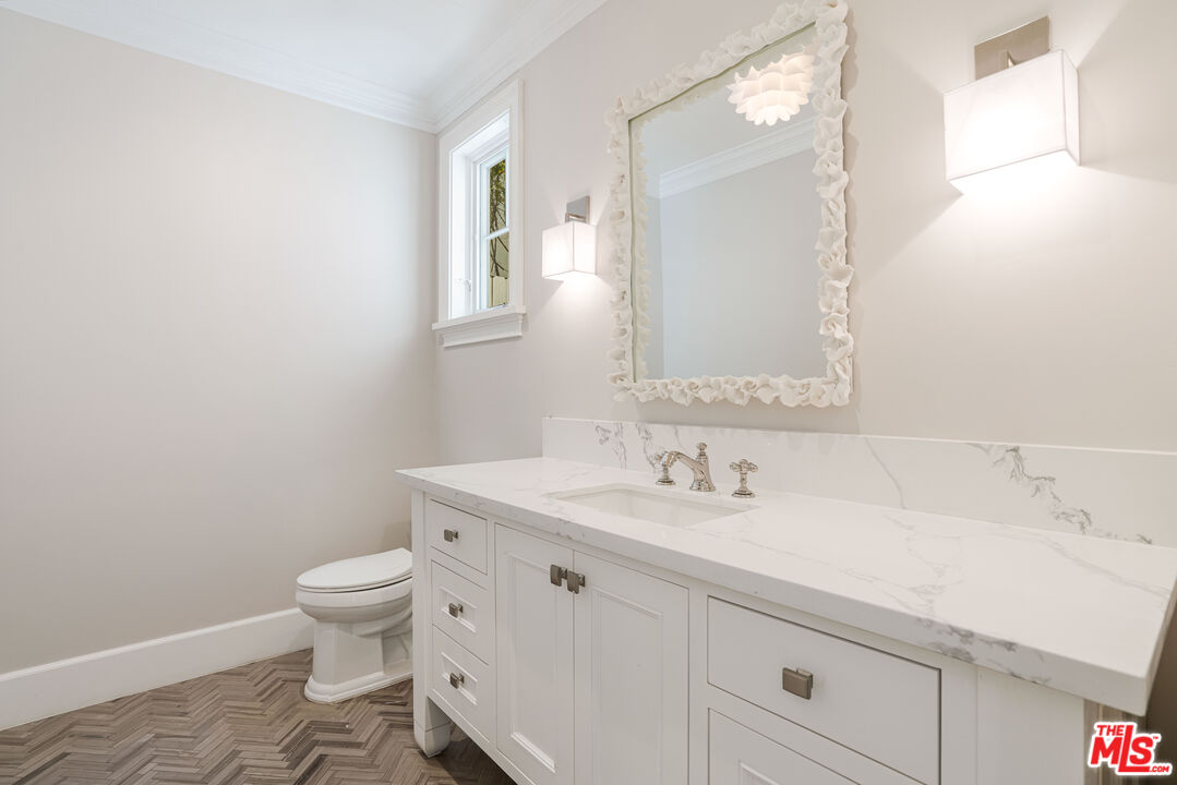 Bathroom with a long marble vanity, floral-framed mirror, brass fixtures and herringbone floor tile.