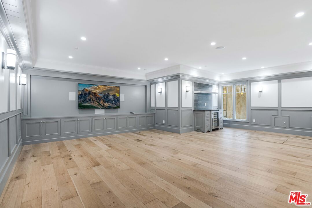 Spacious empty room with gray paneled walls, light wood floors, and a built-in wet bar.