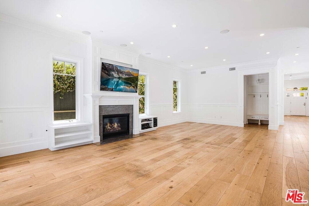 Unfurnished living room with wide-plank wood floors, white paneling, and a built-in fireplace.
