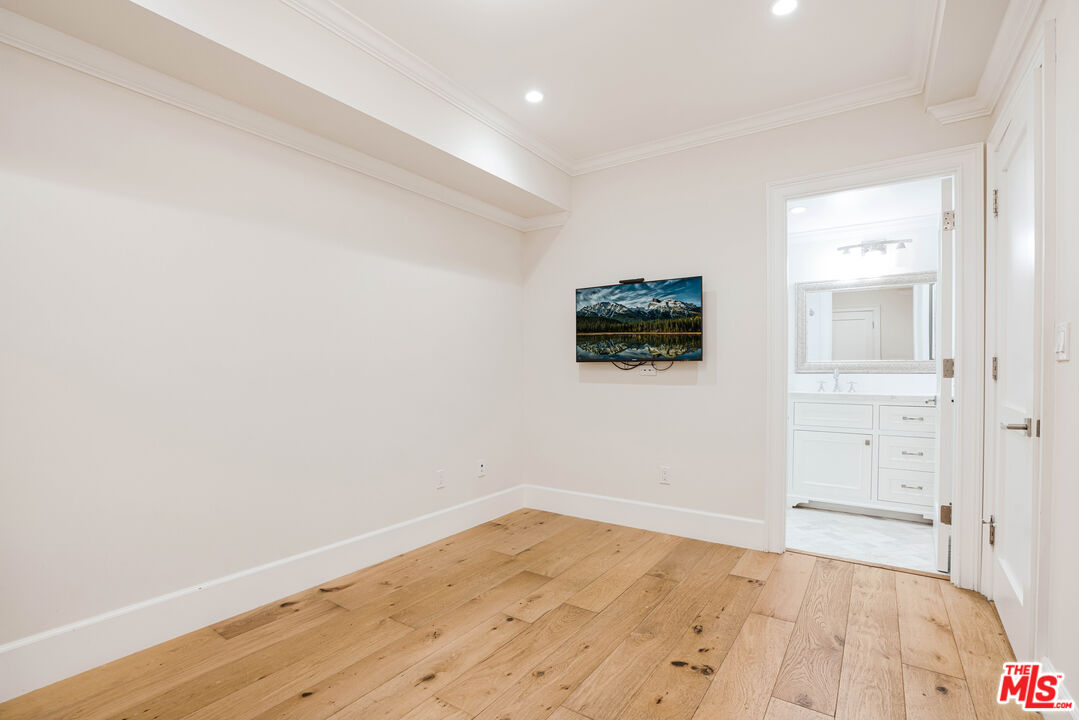 Unfurnished bedroom with wide-plank wood flooring, a wall-mounted television, and an adjoining white bathroom.
