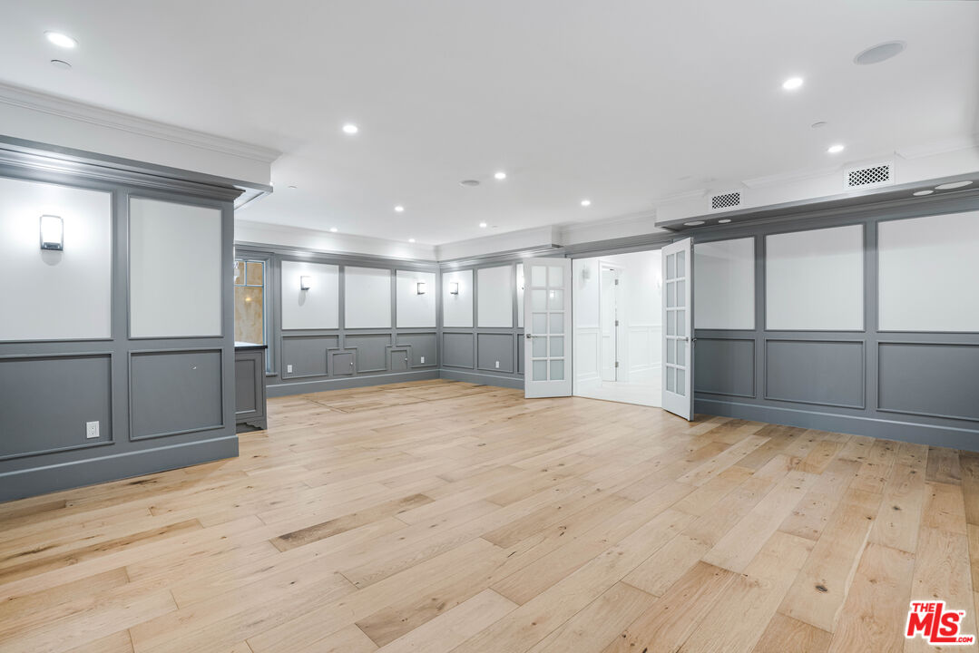 Vacant room with wide-plank wood floors, gray paneled walls, and open French doors.