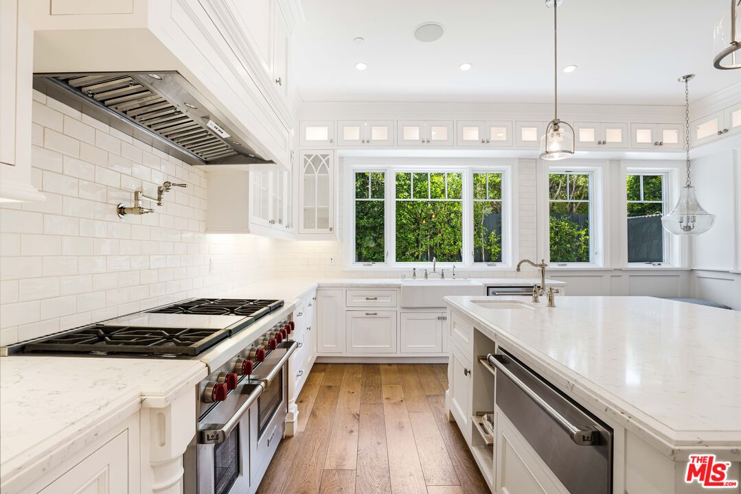White kitchen with a large marble island, stainless-steel appliances, and wide windows overlooking greenery.