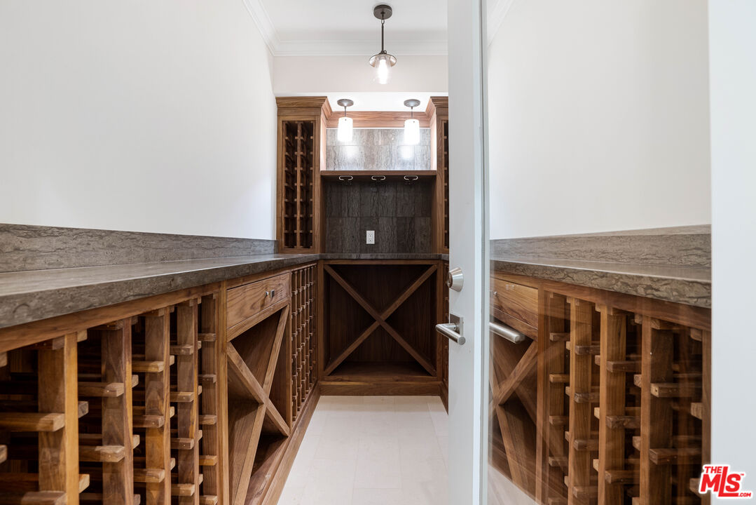 Wine cellar with extensive wooden wine racks, stone counters, and a glass door.