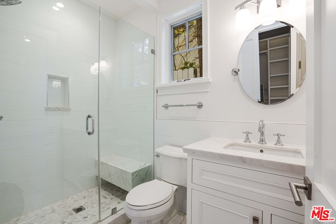 White bathroom with glass shower, built-in marble bench, and marble-topped vanity.