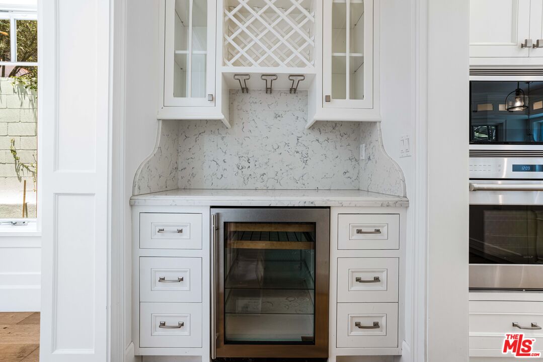 Kitchen beverage station with a glass-front refrigerator, marble backsplash, and lattice wine storage.
