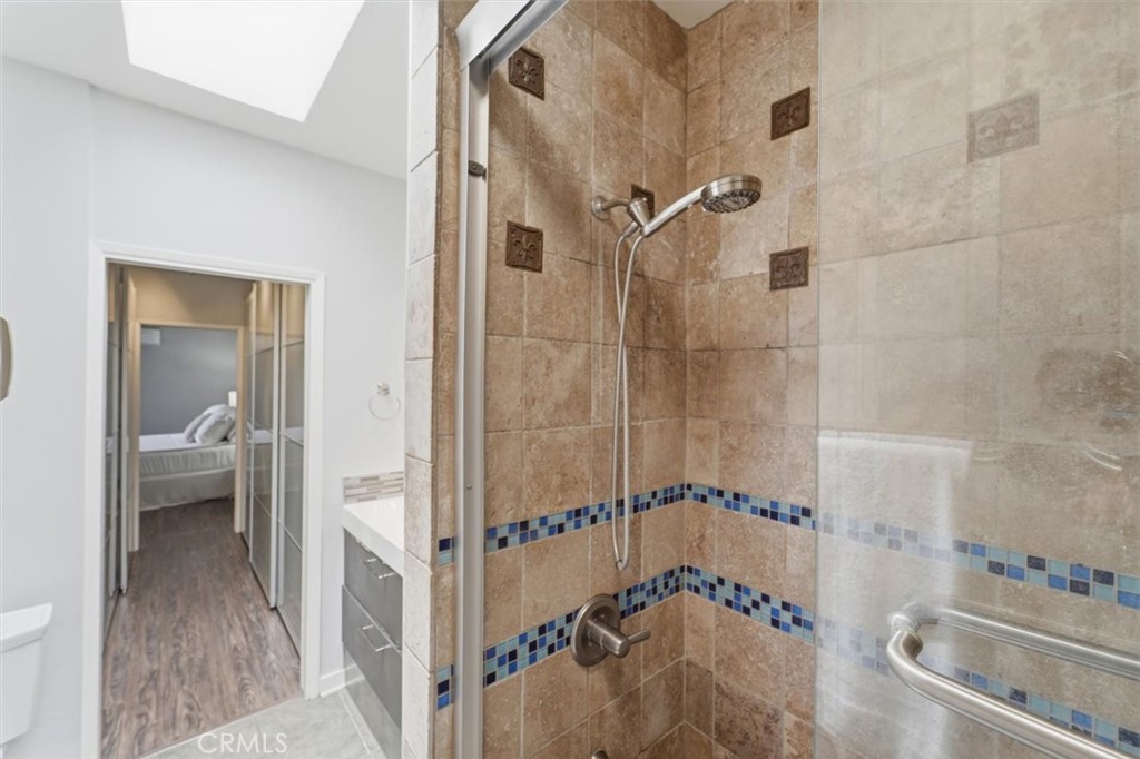 Tiled shower with blue mosaic accent bands, a handheld showerhead, and a metal grab bar.