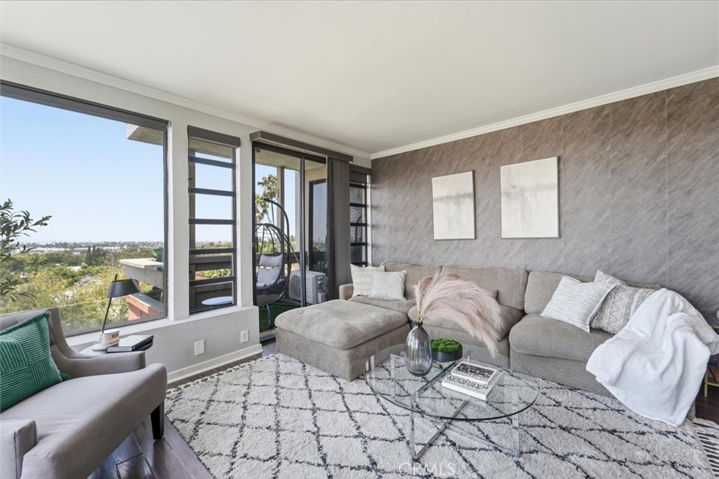 Living room with a gray sectional, patterned rug, and large windows overlooking trees and distant buildings.