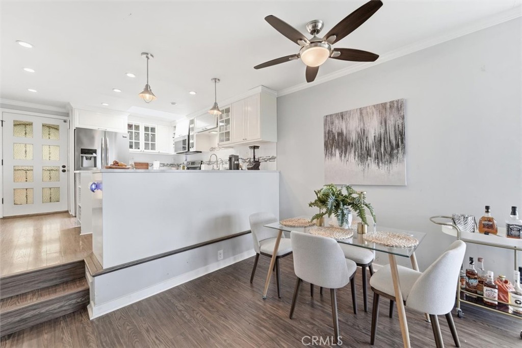Kitchen and dining area with a white peninsula, glass table, and ceiling fan.