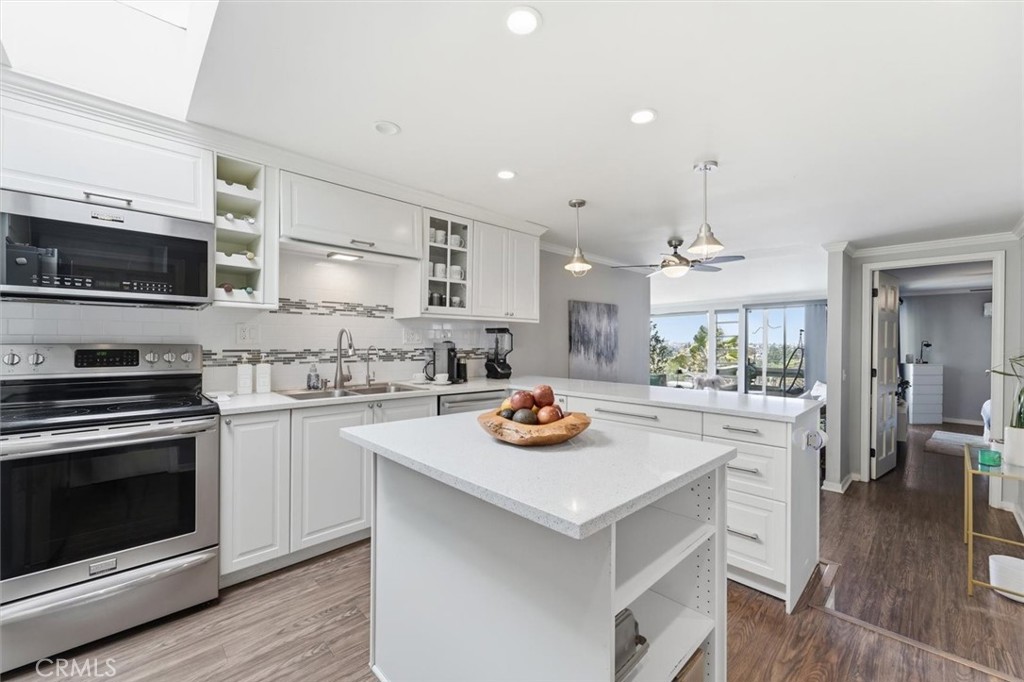 Bright white kitchen with a large island, stainless steel appliances, and sliding glass doors to the living area.
