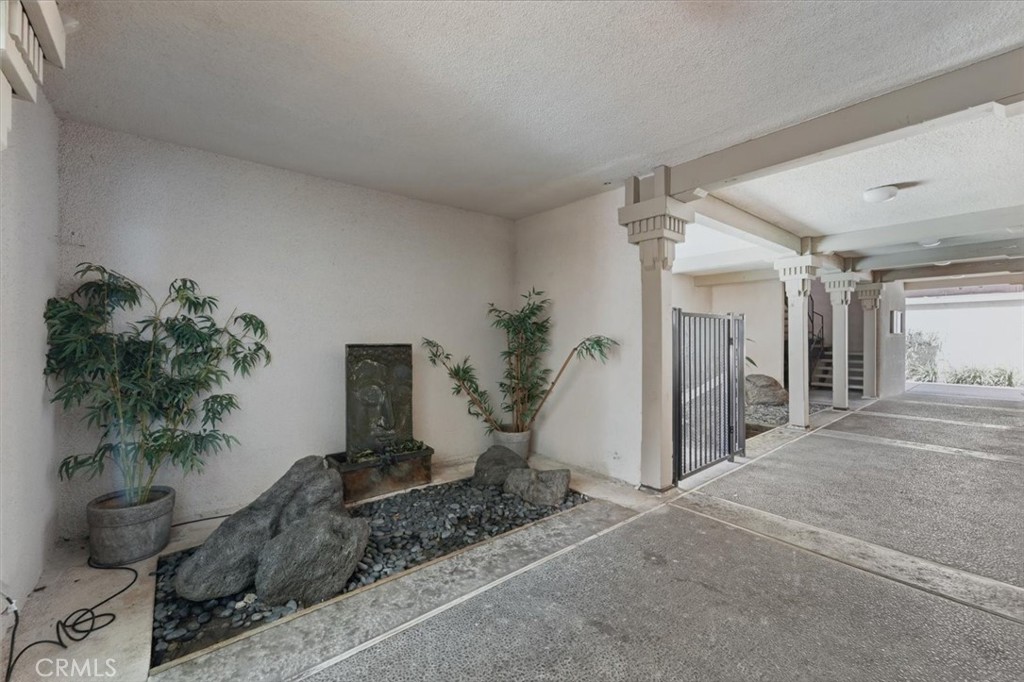 Covered residential walkway with a rock fountain, potted plants, and decorative columns.