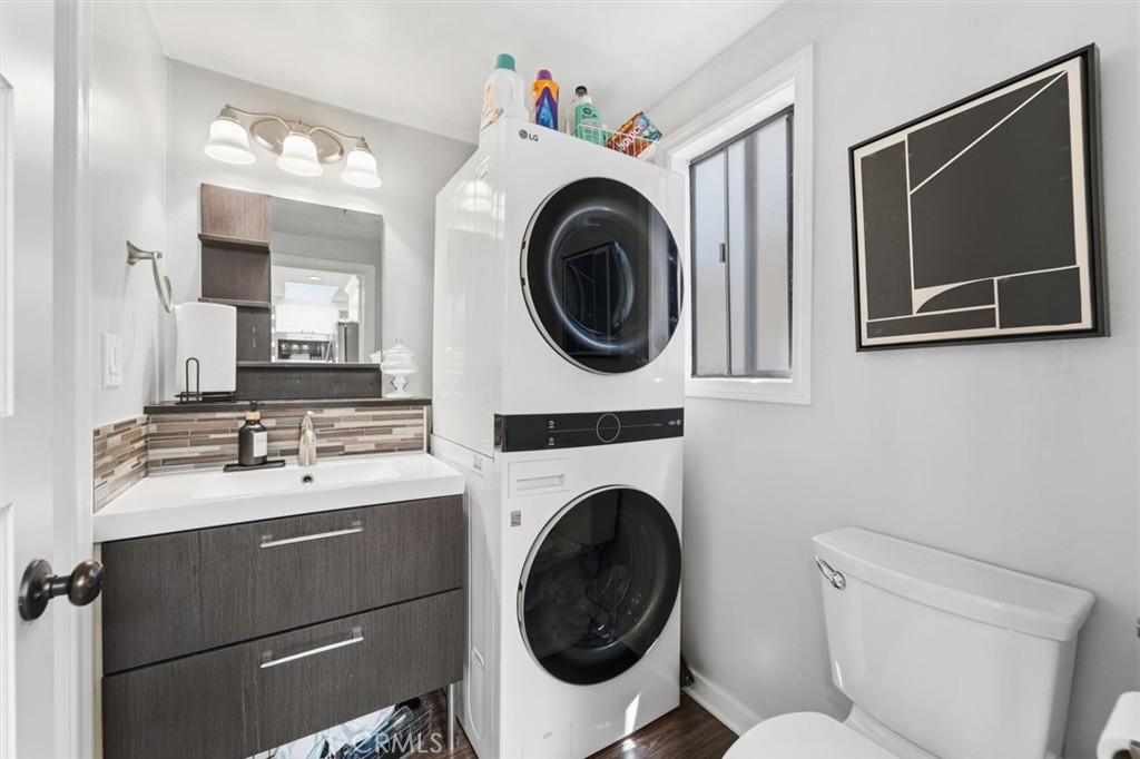 Bathroom with stacked washer and dryer, dark wood vanity, tiled backsplash, and framed abstract artwork.