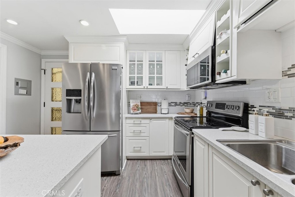 Kitchen with white cabinetry, stainless steel appliances, quartz counters, and gray wood-look flooring.