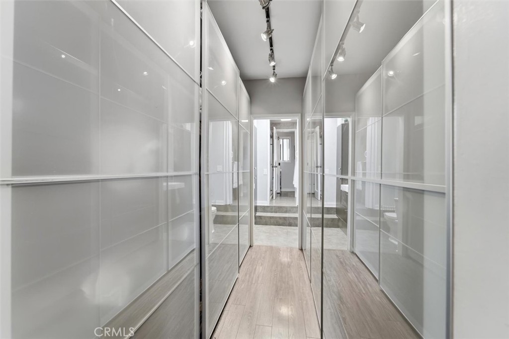Walk-in closet with mirrored wardrobes, wood-look flooring, and track lighting.