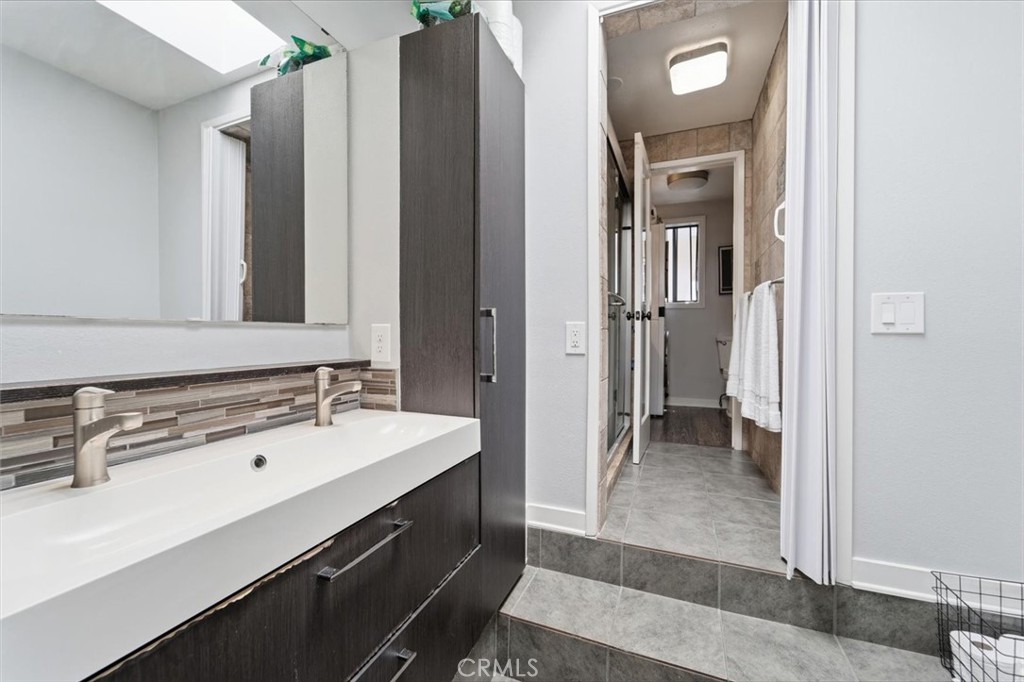Bathroom with a double-sink vanity and dark cabinetry beside a tiled bathing area.