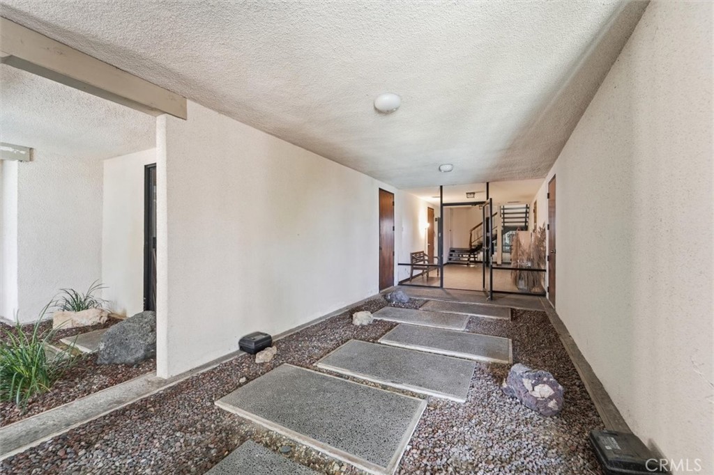 Covered building entry with concrete stepping stones across gravel leading to glass doors.
