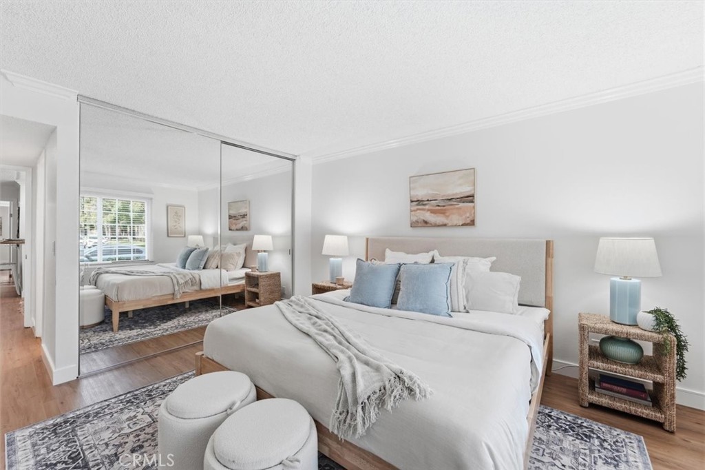 Staged bedroom with a white bed, blue pillows, mirrored closet doors, and two round stools.