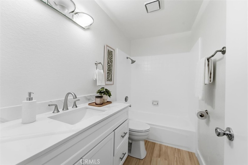 Bathroom with a white vanity, tub-shower combination, and warm wood-look flooring.