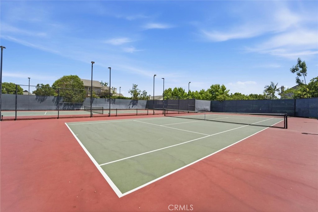 Outdoor tennis court with a green surface, red pavement, and fenced neighboring courts.