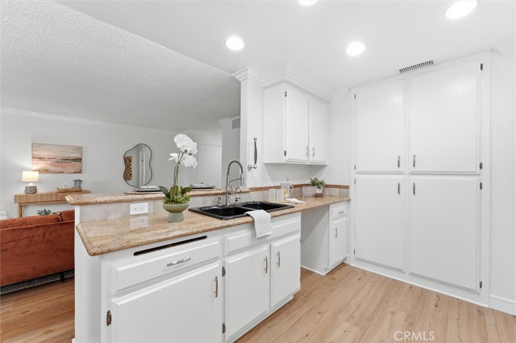 Kitchen with white cabinetry, tan stone counters, black sink, and breakfast bar opening to the living area.
