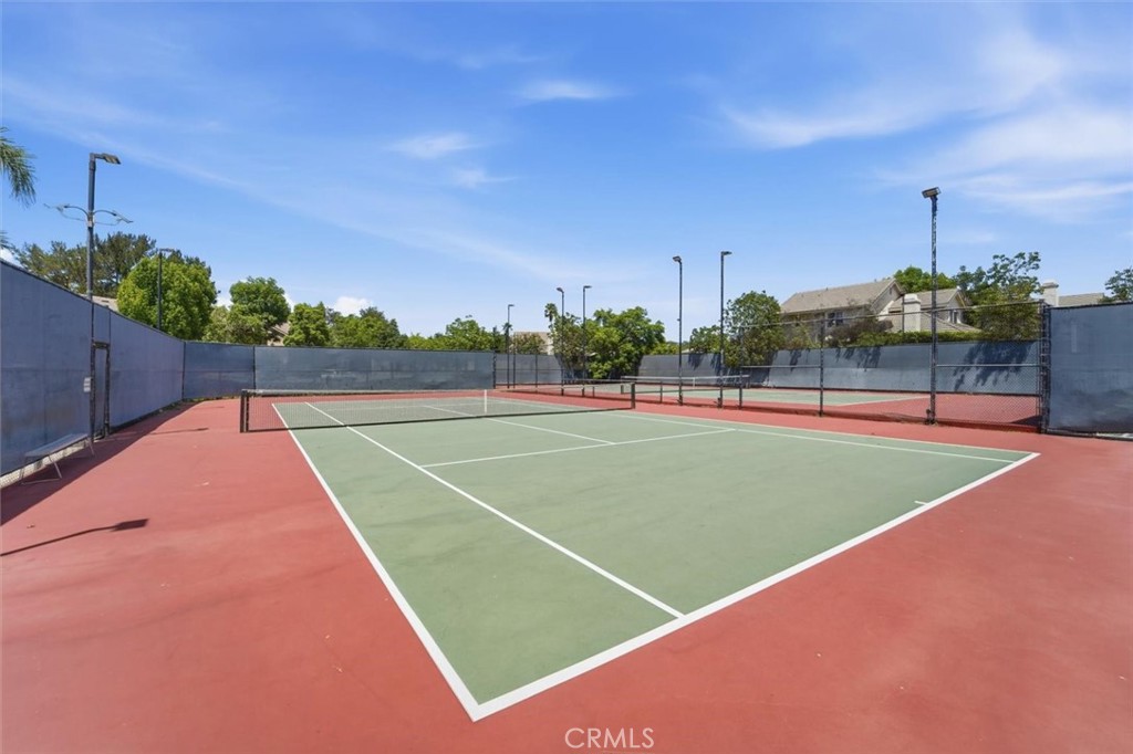 Tennis court with a green playing surface, red surrounds, and tall perimeter fencing.