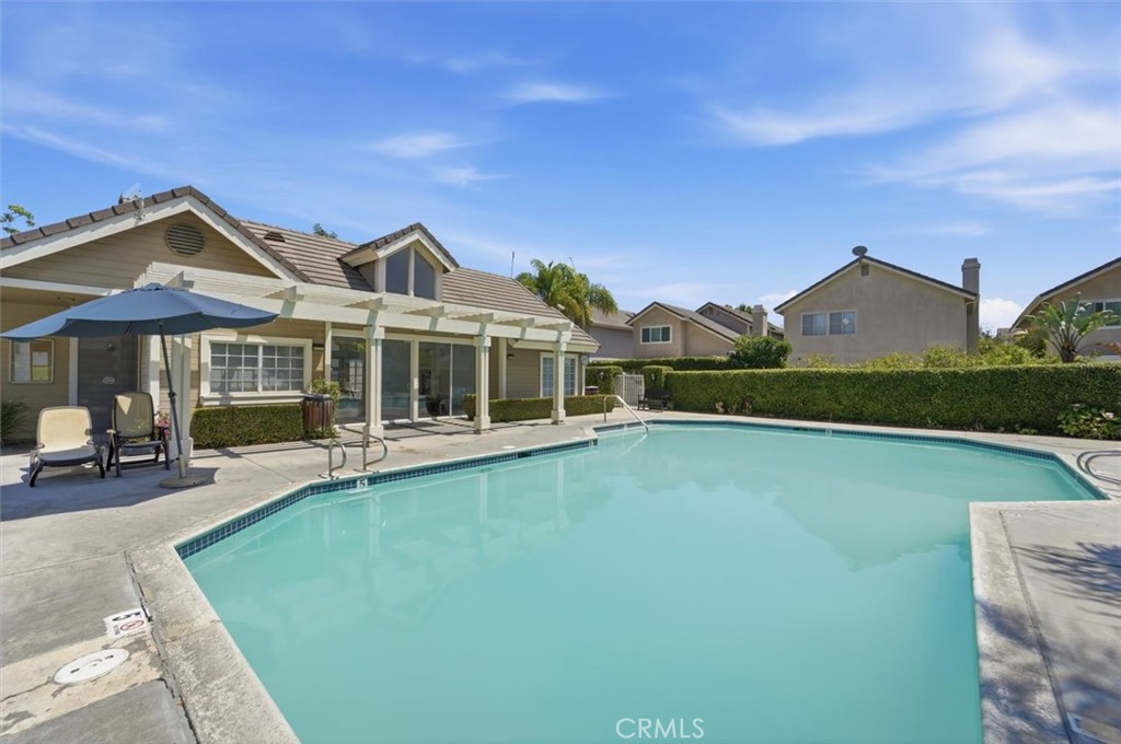 Backyard swimming pool beside a single-story home with a covered patio and shaded seating.
