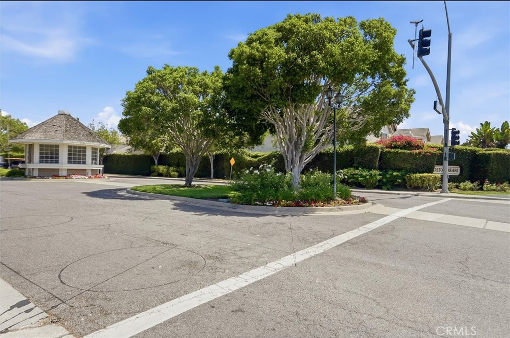 Residential entrance with a white guardhouse and a landscaped island beneath mature trees.