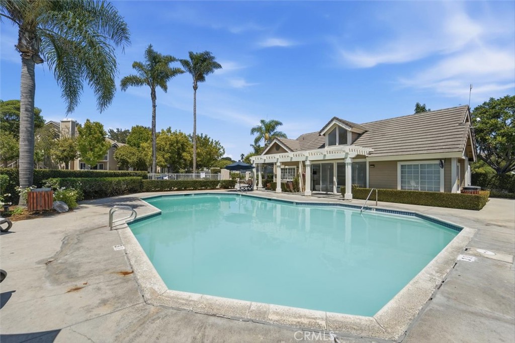 Swimming pool beside a clubhouse, with a pergola and palm trees.