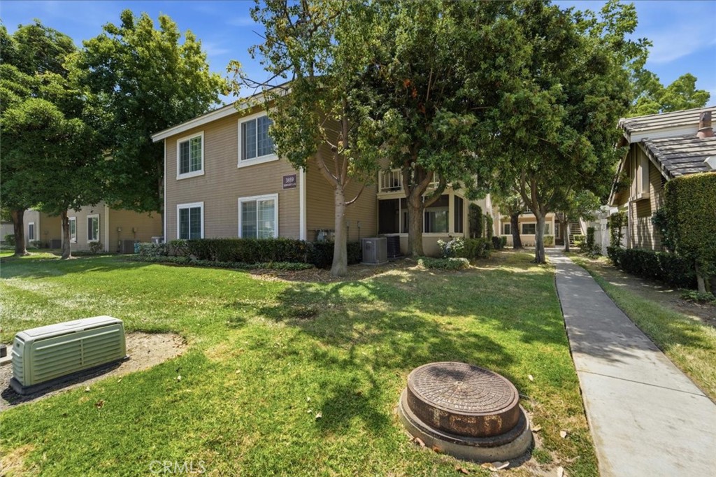 Two-story tan residential building in a leafy complex, with a front lawn and walkway.