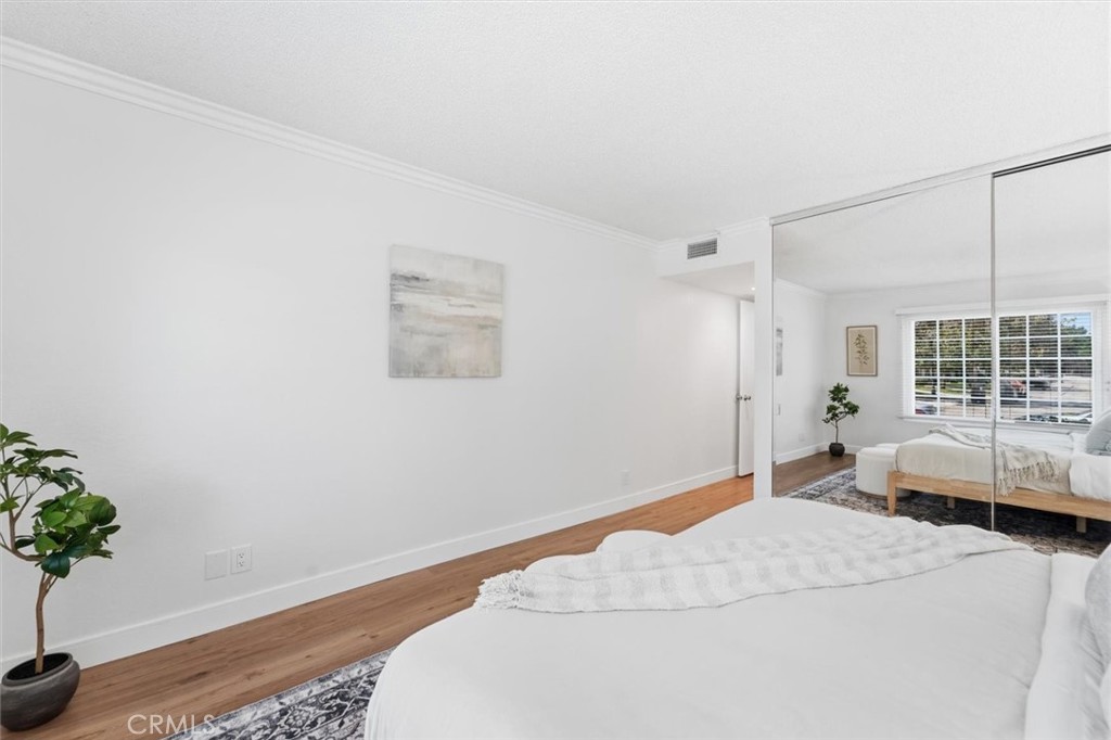 Staged bedroom with a large white bed, mirrored closet doors, and warm wood flooring.