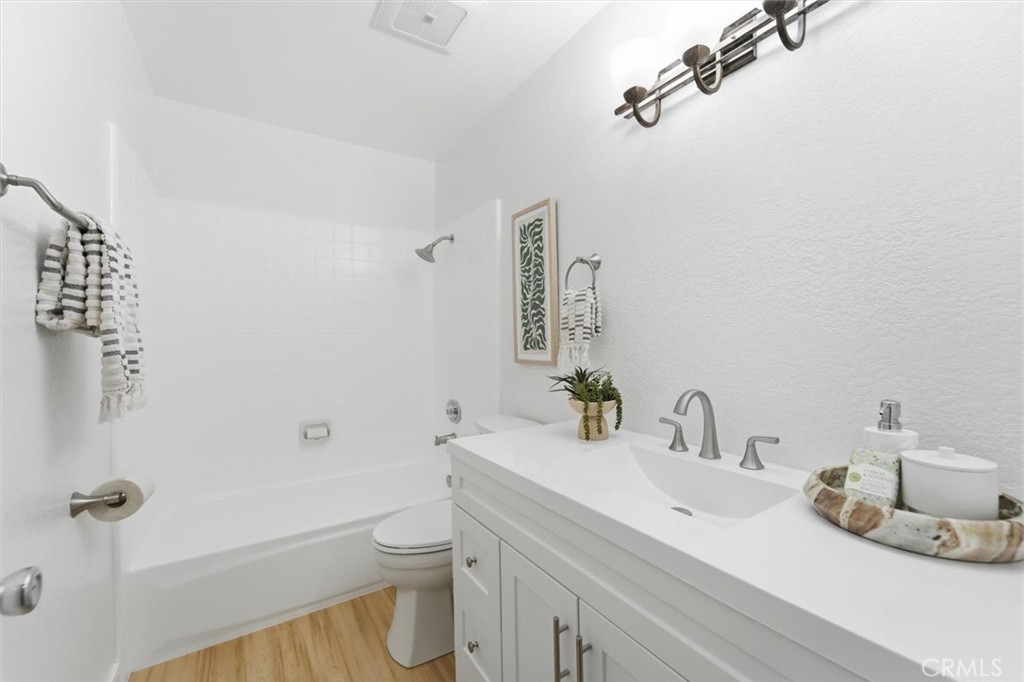 Bright bathroom with a white bathtub and shower beside a single-sink vanity.