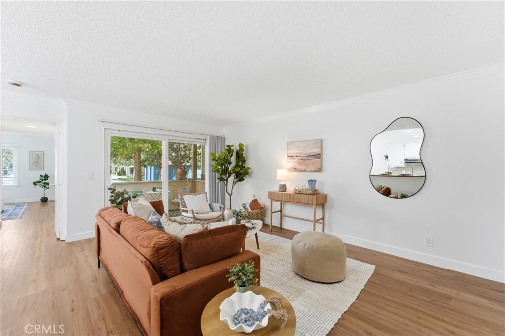 Staged living room with a rust-colored sofa, wood floors, and a large window overlooking trees.