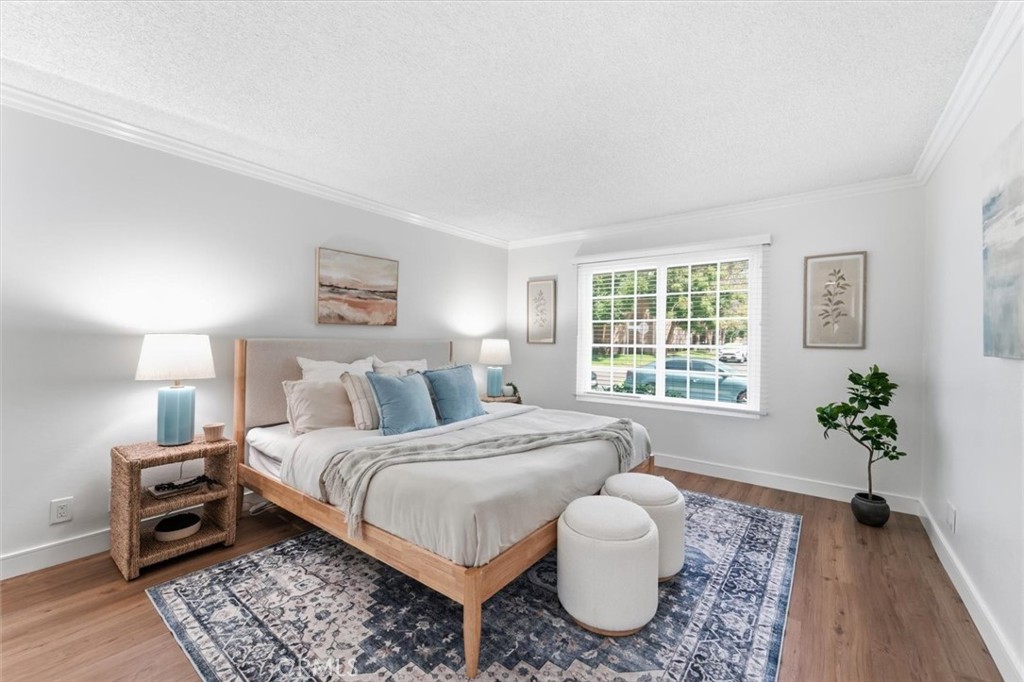 Staged bedroom with a white bed, blue pillows, patterned rug, and window overlooking greenery.