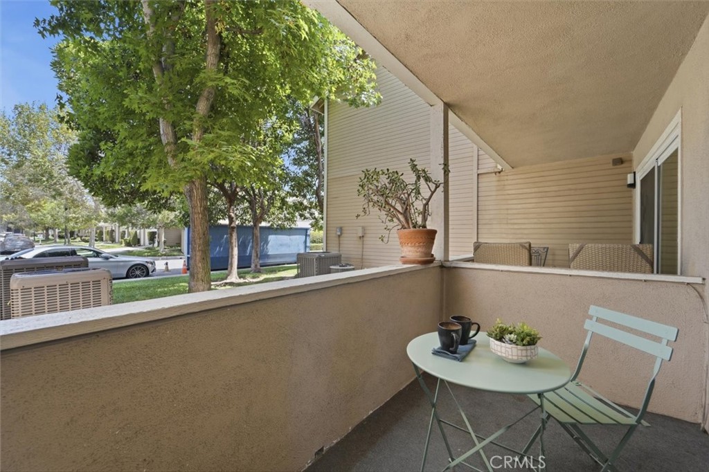 Covered patio with a pale green bistro set, coffee cups, and a succulent overlooking leafy trees.