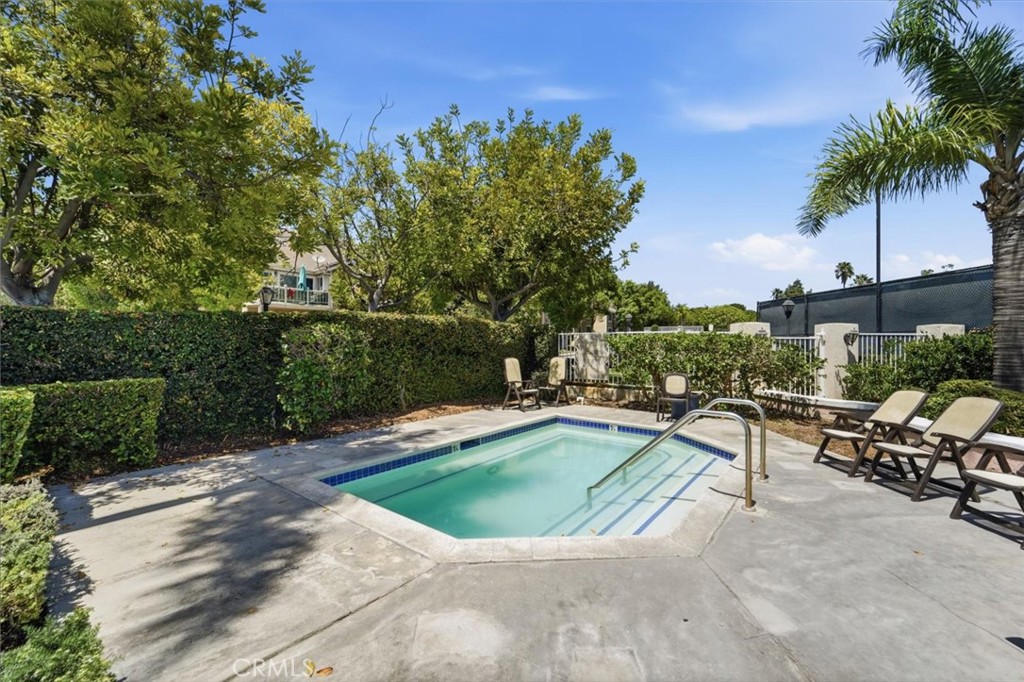 Outdoor pool with shallow-entry steps, lounge chairs, and leafy hedges.