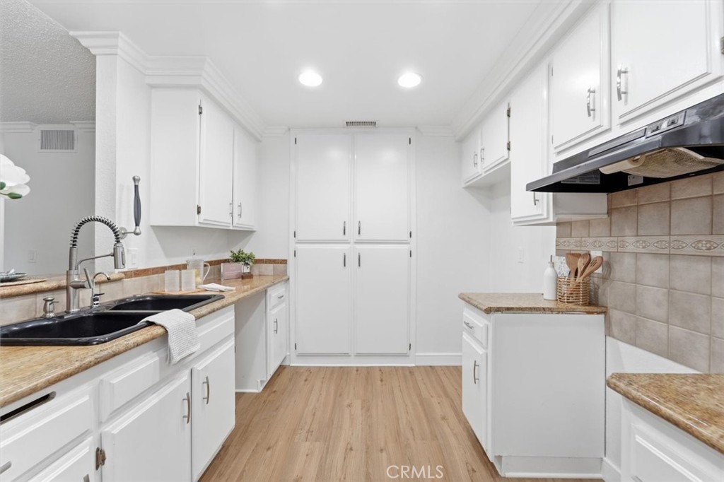 Bright white kitchen with a black double sink, tan countertops, and light wood flooring.