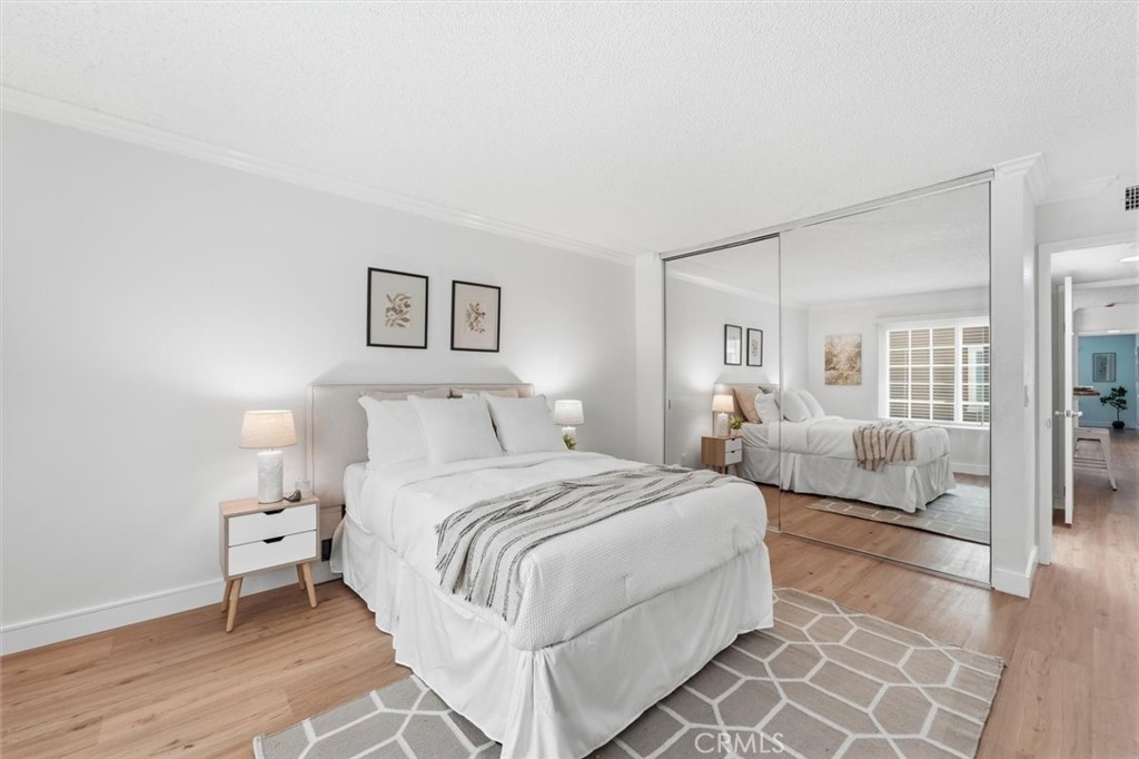 Staged bedroom with a white bed, light wood floors, and mirrored closet doors.