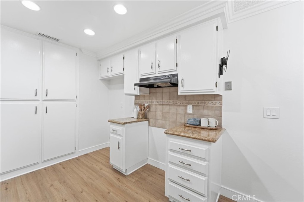 Kitchen with white cabinetry, tan tile backsplash, and light wood-look flooring.