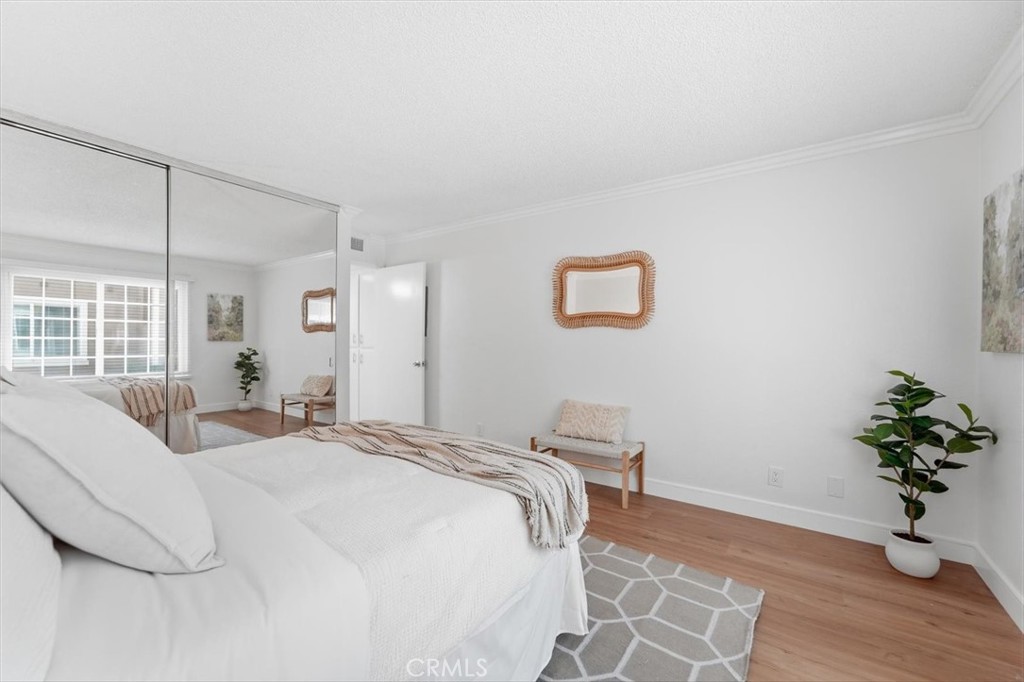 Staged bedroom with mirrored closet doors, a white bed, and warm wood flooring.