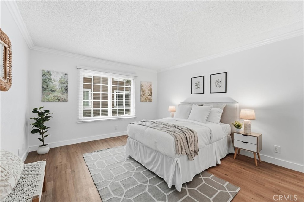 Staged bedroom with a white upholstered bed, geometric rug, and large window with blinds.