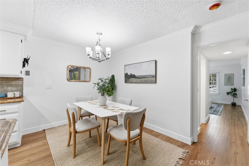 Staged dining room with a white table, four upholstered chairs, woven rug, and chandelier.