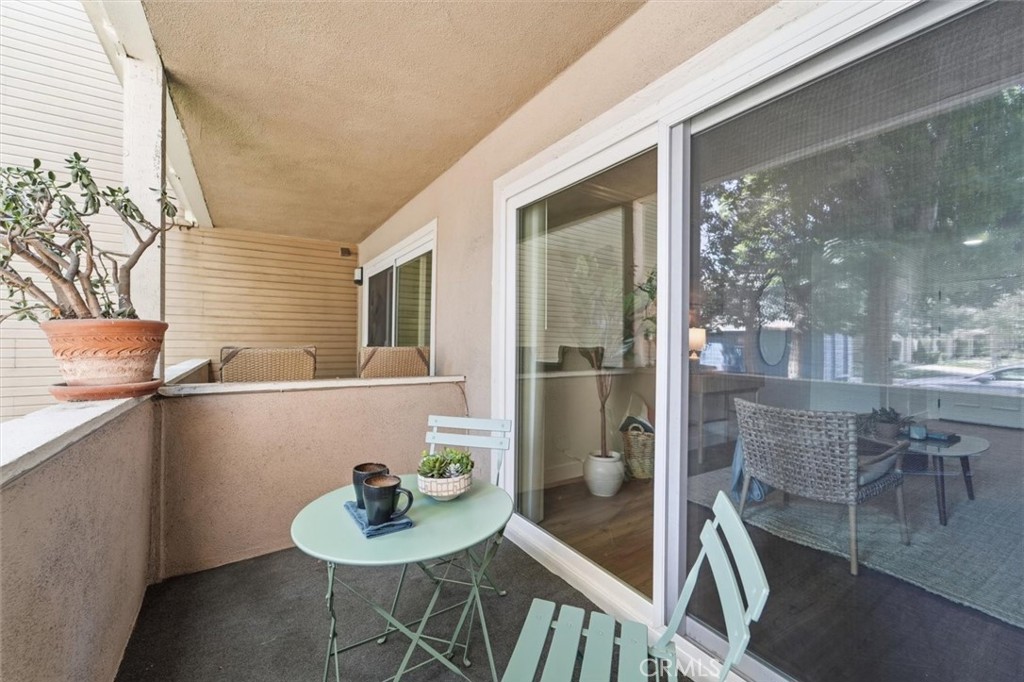 Covered balcony with mint-green bistro furniture and potted plants beside sliding glass doors.