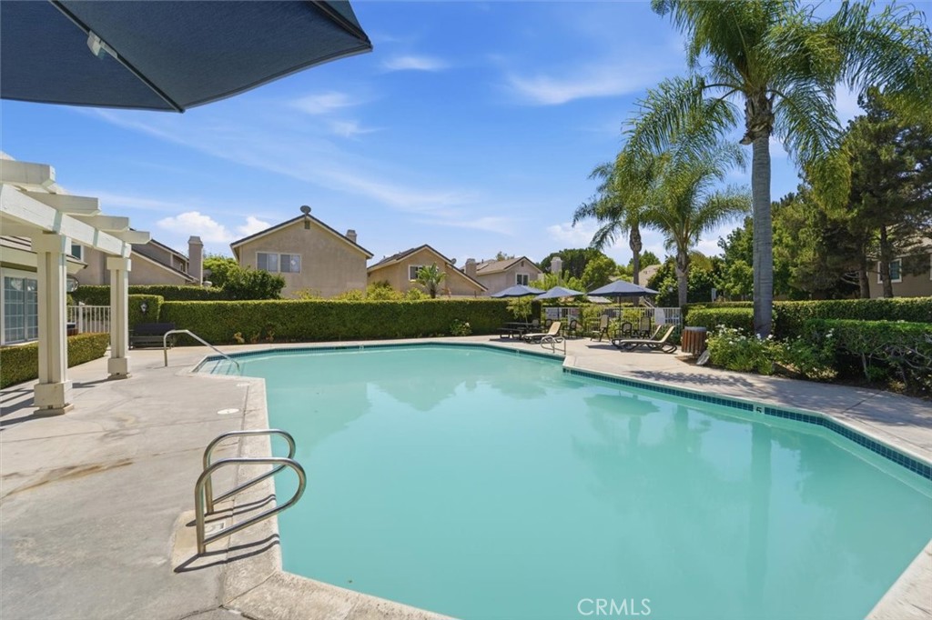 Swimming pool with lounge seating, patio umbrellas, and palm trees.