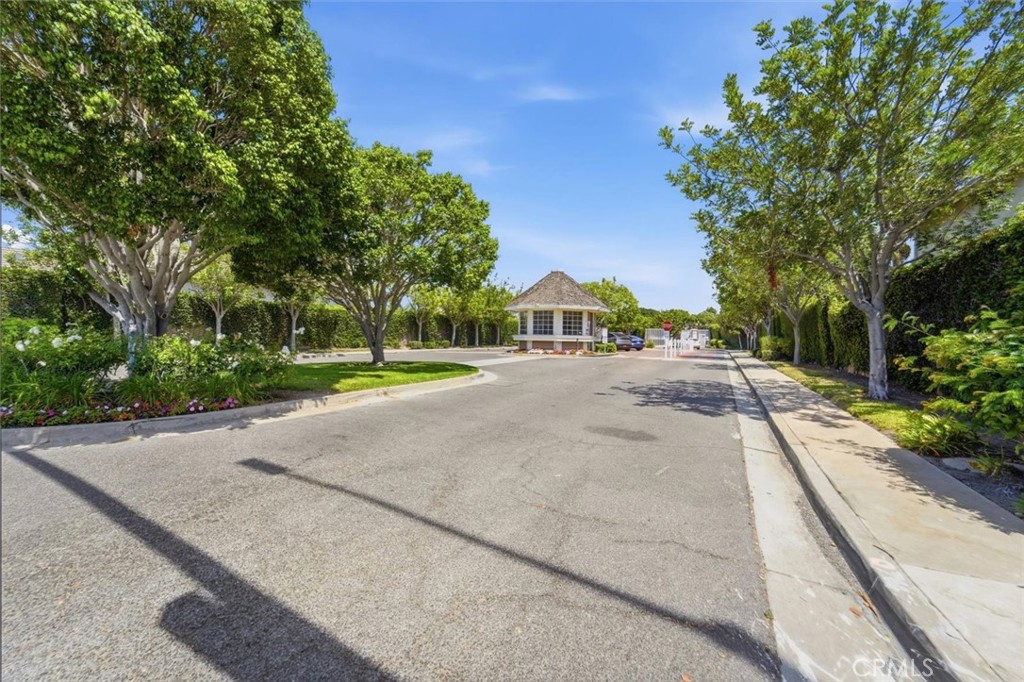 Tree-lined residential street leading to a gated entrance and guardhouse.