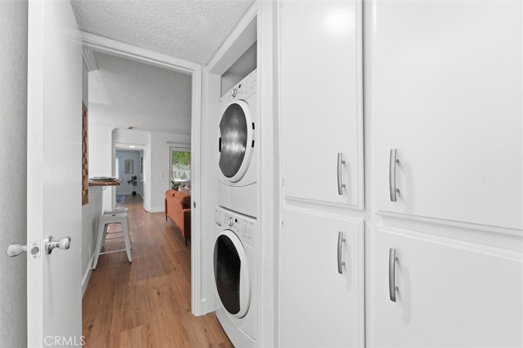 Laundry area with stacked washer and dryer beside a hallway opening onto a living room.