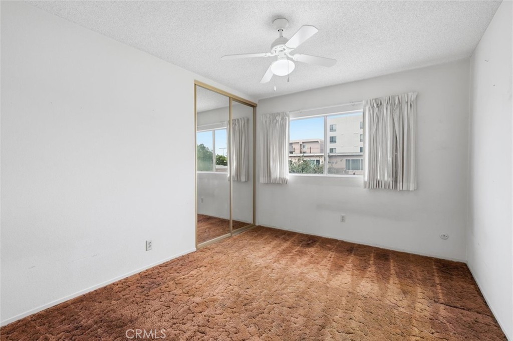 Empty bedroom with rust-colored carpet, mirrored closet doors, and a curtained window.