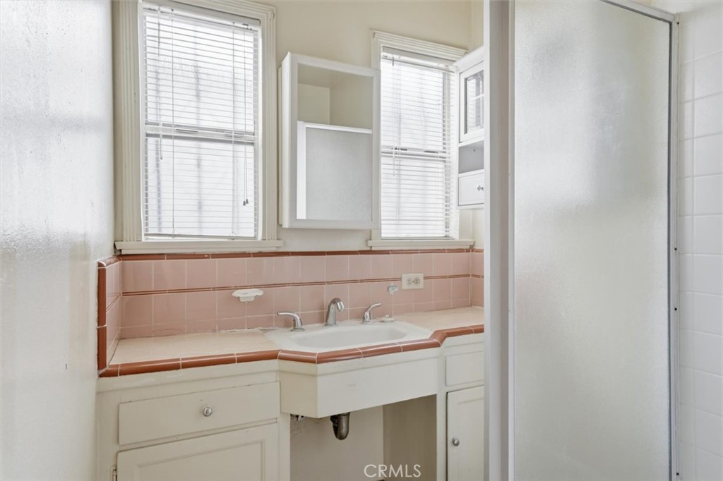 Bathroom with a built-in white sink, pale pink tile, and two windows with blinds.