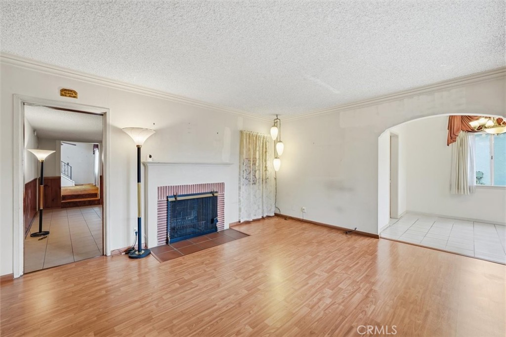Unfurnished living room with wood flooring, a brick-trimmed fireplace, and an arched opening to a tiled room.